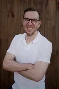 Man in a white polo and glasses smiles.