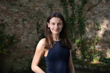 Woman in dark tank top smiles, brick wall backdrop.