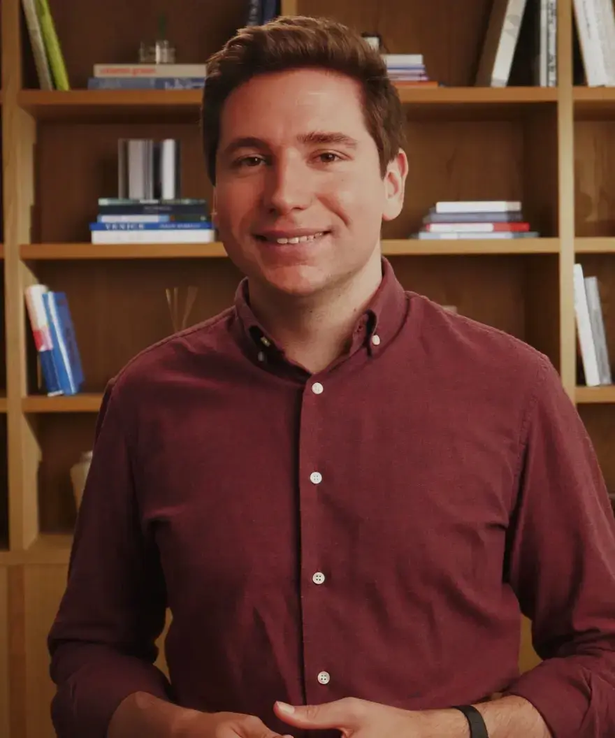 Man in red shirt smiles in front of bookshelf.