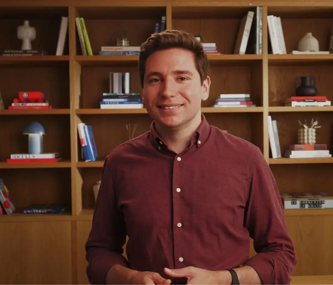 Man in maroon collared shirt in front of bookshelf