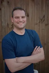 Man in a blue t-shirt with arms crossed, smiling.