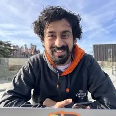 Man with beard and hoodie smiling at camera.