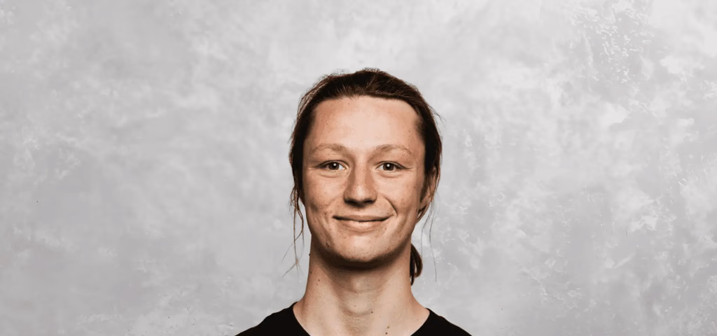 Young person with long hair smiling against a textured background.