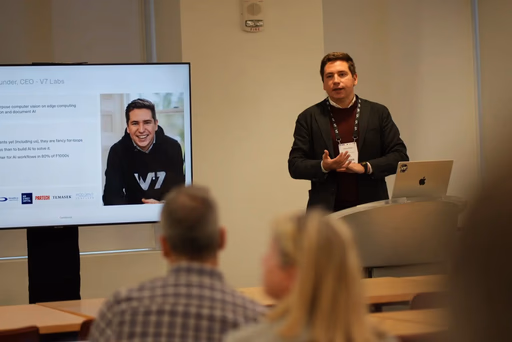 Man presenting at a conference beside a screen showing a smiling person.