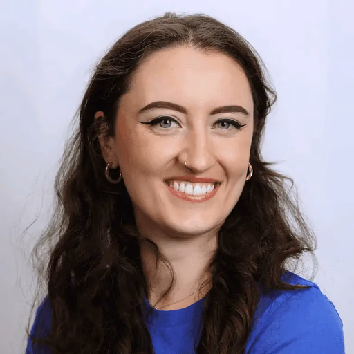 Woman with long dark curly hair and blue shirt smiling.