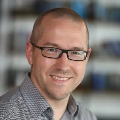Man wearing glasses, smiling, with short hair.