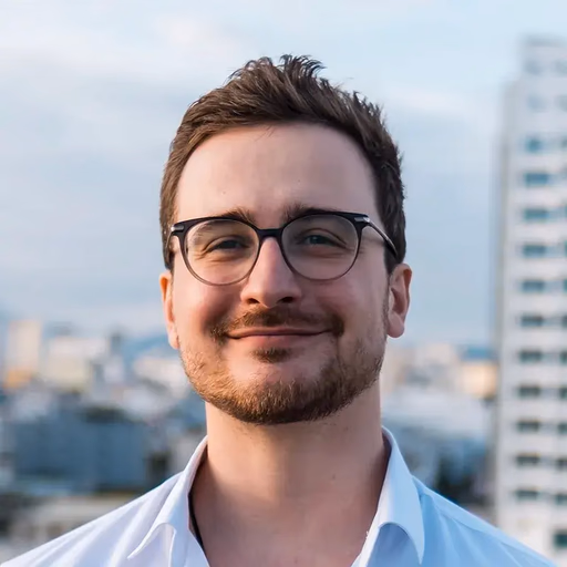 Man with glasses and beard smiling outdoors.