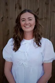 Woman in white shirt smiling by wooden fence.