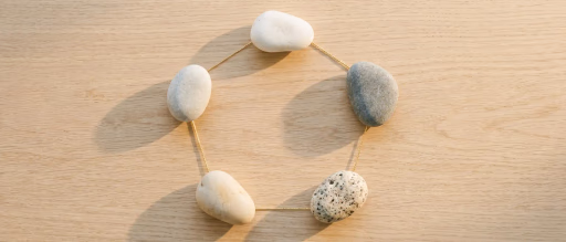Five stones connected by gold wire in a pentagon on wood.