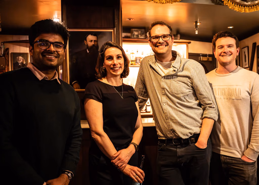 Four people smiling in a bar with paintings on the wall.