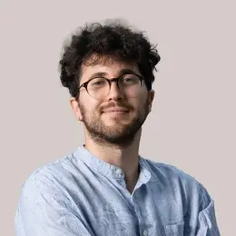 Man with glasses and curly hair smiles.