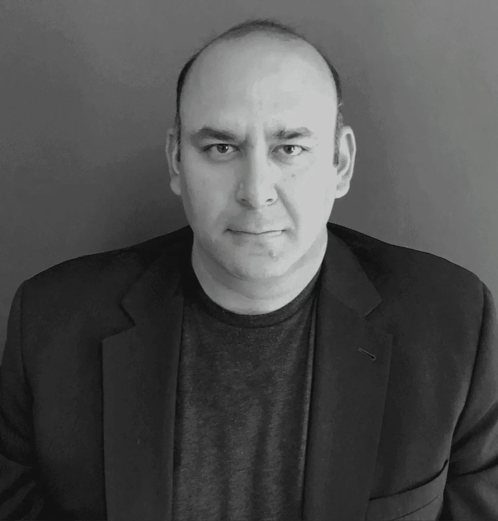 Man wearing a suit jacket and dark shirt, looking directly at the camera.