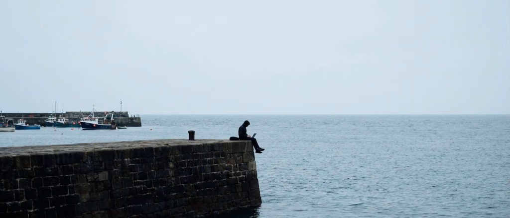 Person on pier with laptop facing the ocean.