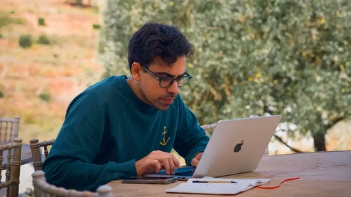 Man with glasses using a laptop outdoors.
