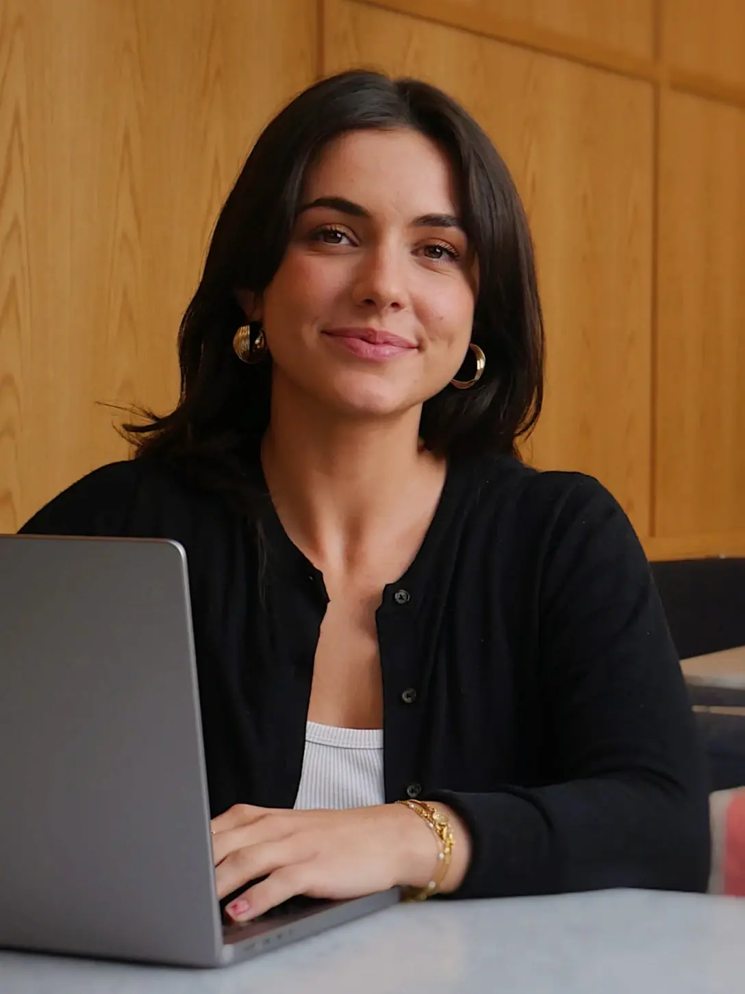 Woman with dark hair smiles at laptop.