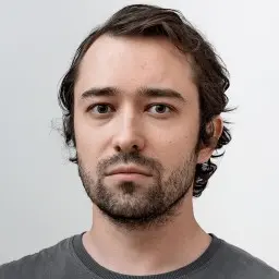Man with dark hair and beard, wearing a grey shirt.
